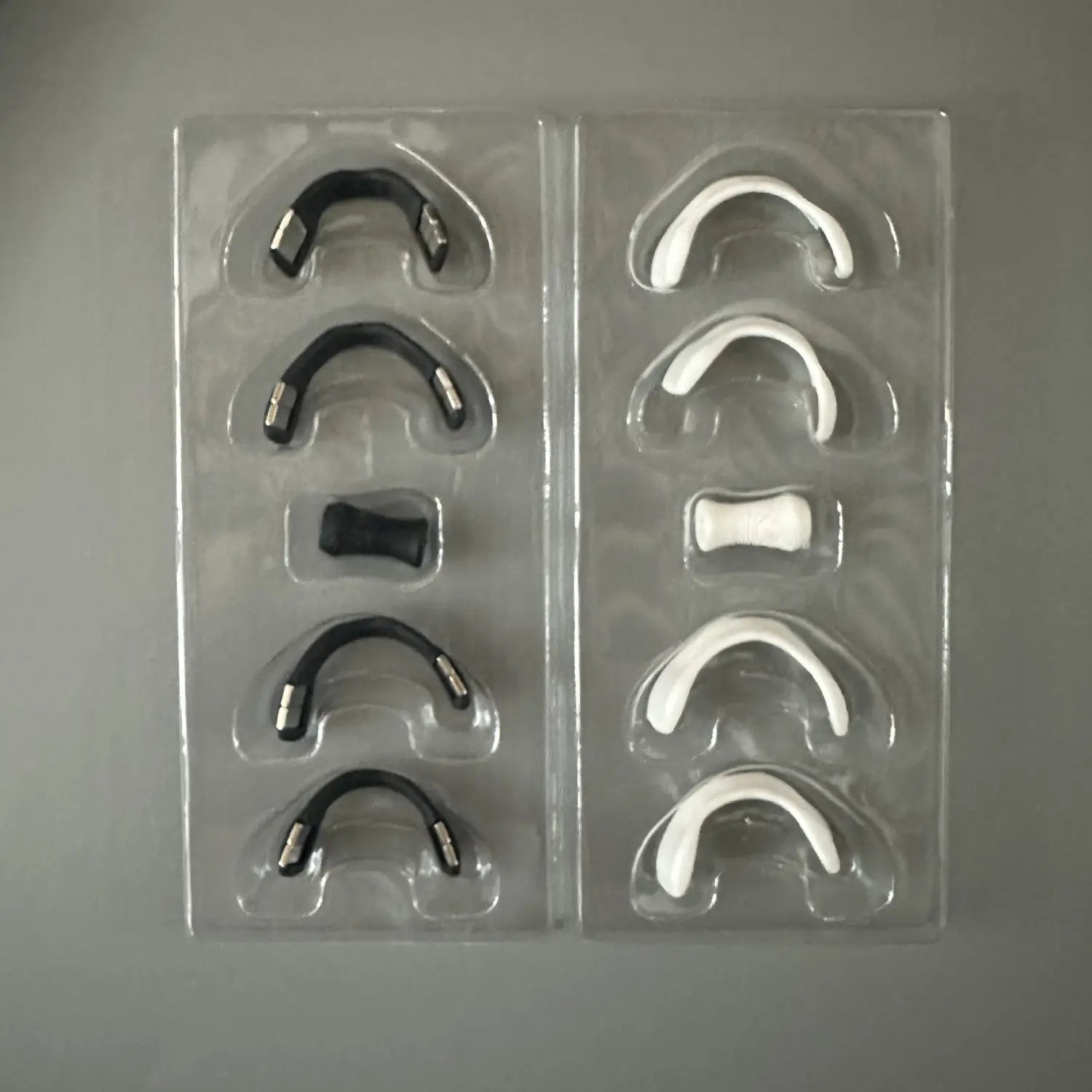 Plastic tray with black and white dental appliances for Magnetic Nasal Strips to enhance sleep quality.